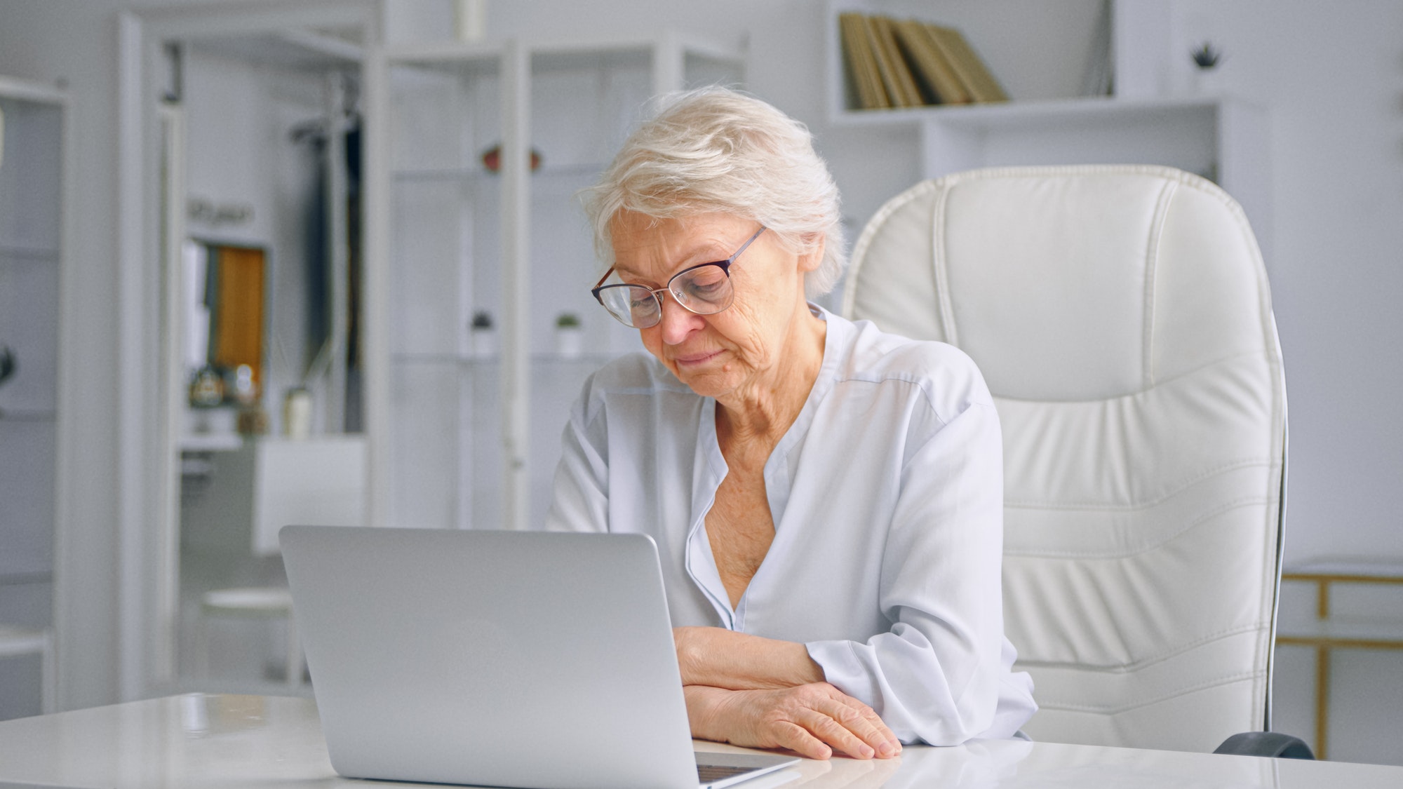 Angry old businesswoman looks around sitting on white chair at table