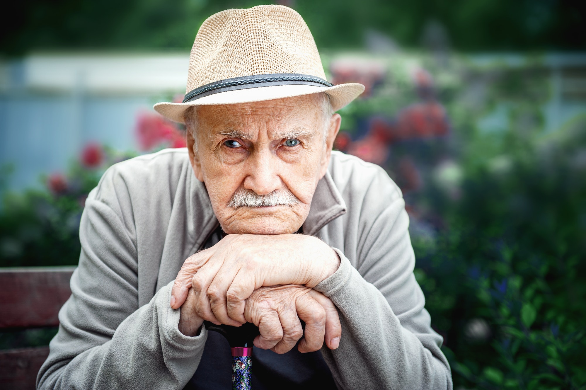 sad, angry old man with a hat is sitting in an open-air garden. concept of loneliness and lonely old