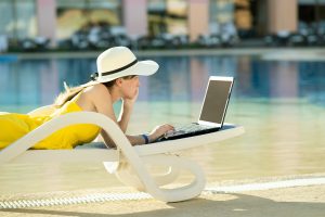 Young woman is lying on beach chair working on computer laptop connected to wireless internet typing