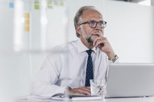 Mature businessman with laptop at desk in office thinking