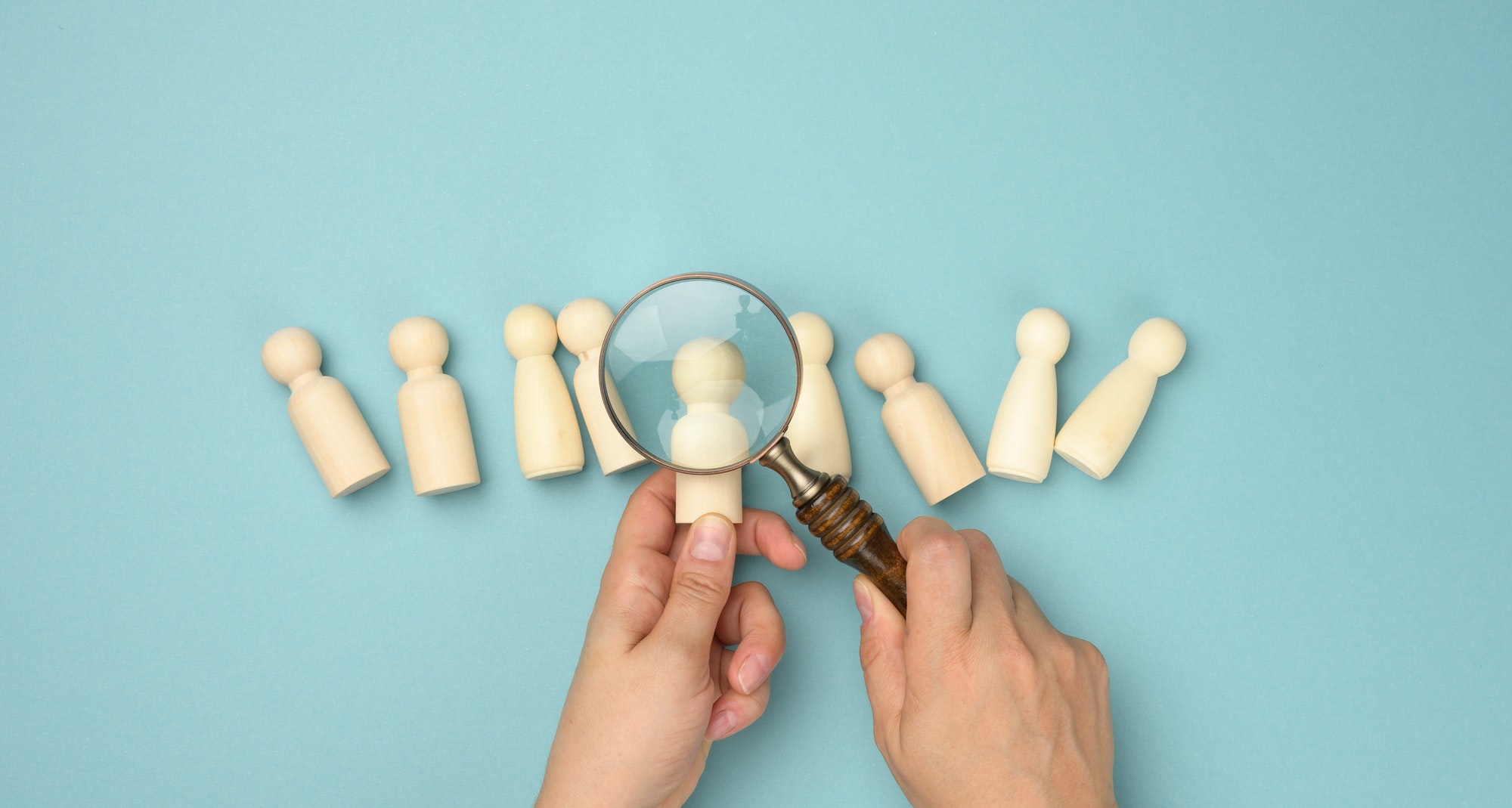 Wooden men and a magnifying glass on a blue background. Recruitment concept