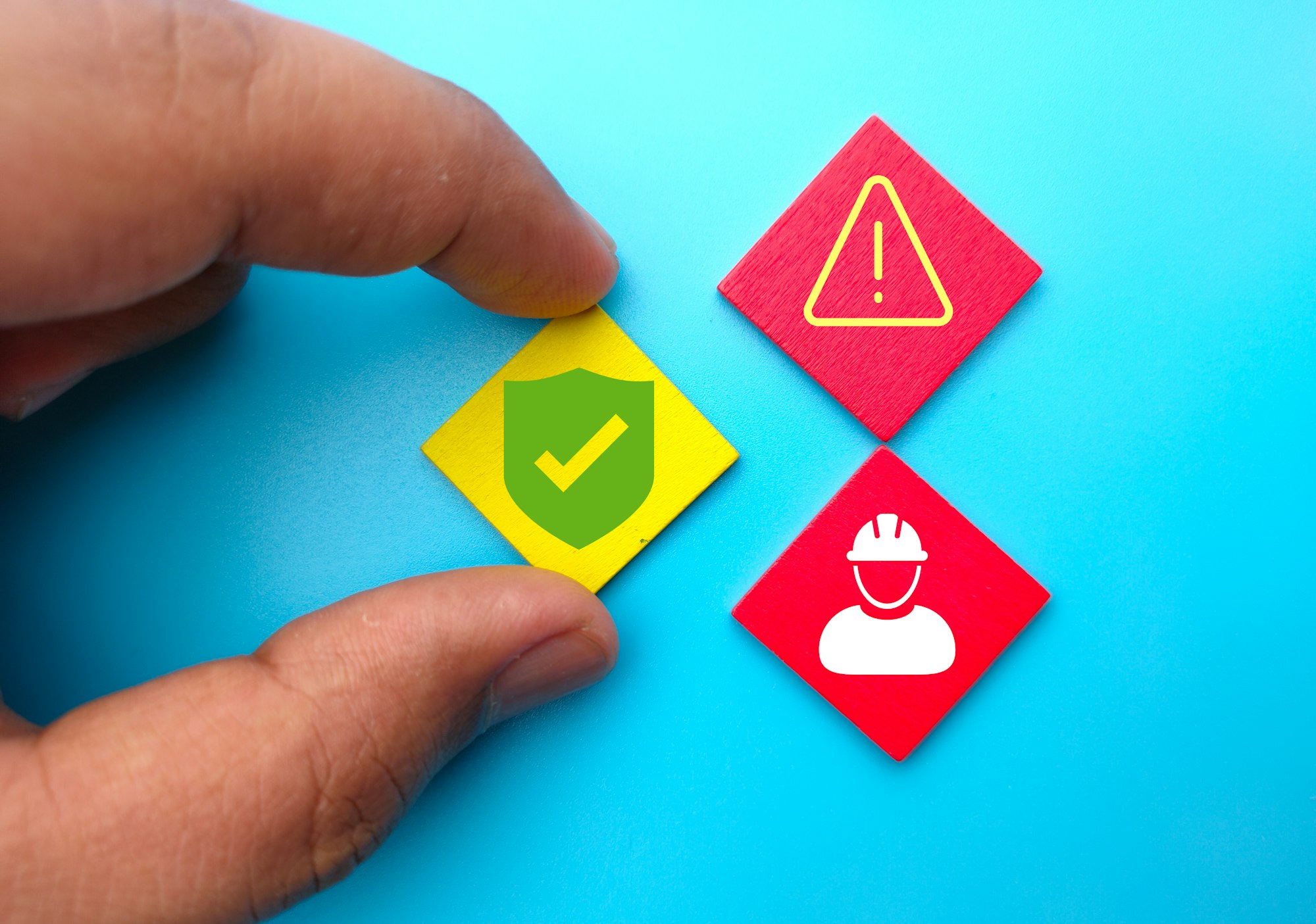 Close-up shot of a hand holding colorful wooden rhombuses with a worker, caution, and safety icons